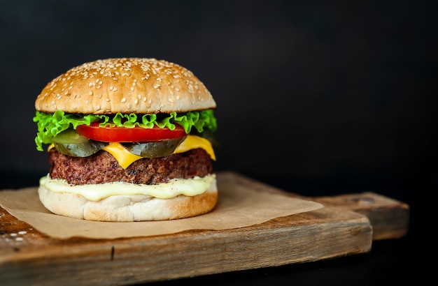 Homemade hamburger with lettuce, tomato, cheese and cucumber on a cutting board  with copy space for your text