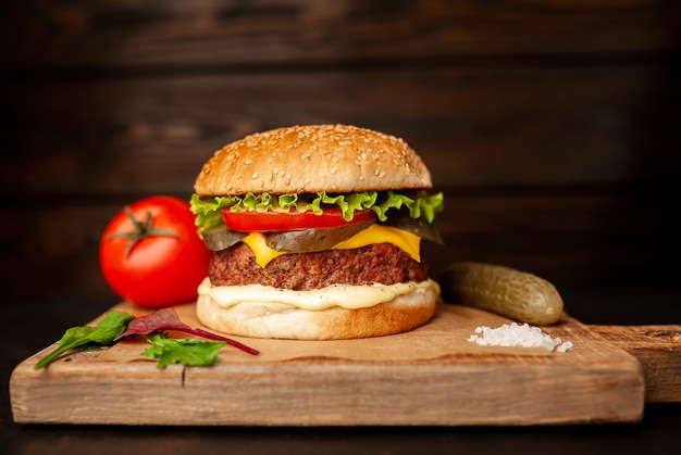 Homemade hamburger with lettuce, tomato, cheese and cucumber on a cutting board