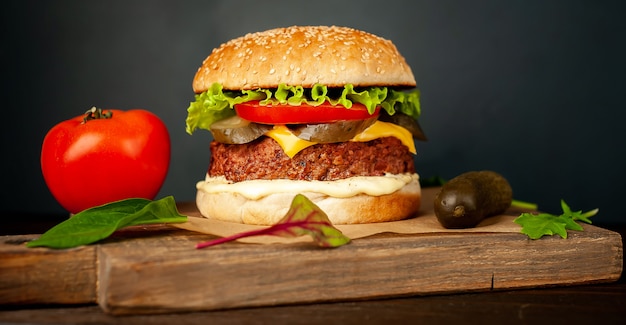 Homemade hamburger with lettuce, tomato, cheese and cucumber on a cutting board