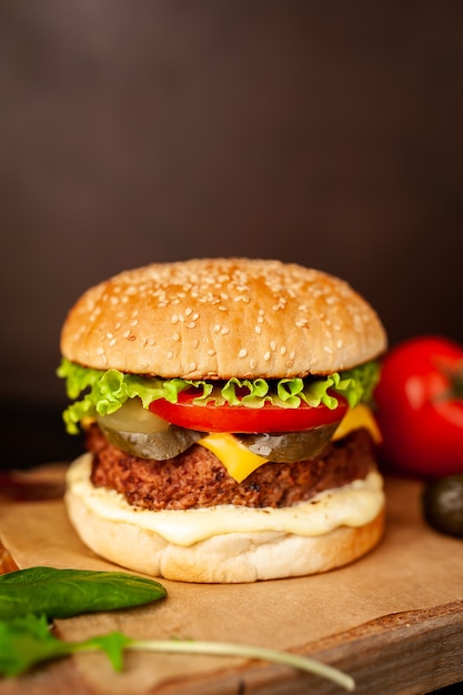 Homemade hamburger with lettuce, tomato, cheese and cucumber on a cutting board