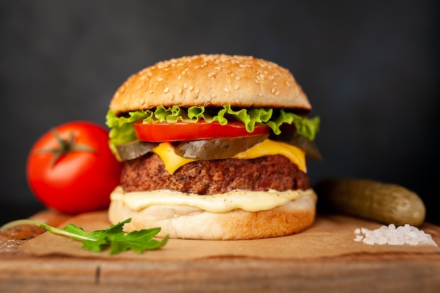 Homemade hamburger with lettuce, tomato, cheese and cucumber on a cutting board