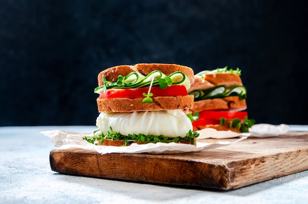 Homemade Healthy Sandwich with Wholegrain Bread, Poached Egg, Cucumber, Tomato and Micro Herbs Watercress Salad on Wooden Board.