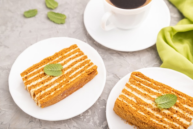 Homemade honey cake with milk cream and mint with cup of coffee on a gray concrete table