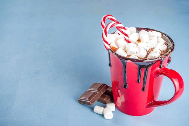 Homemade hot chocolate in red mug, with mini marshmallows and chocolate drips, candy cane decor, copy space