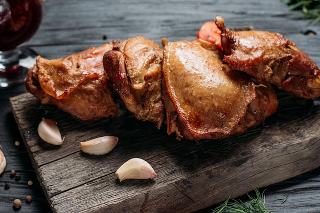 Homemade hotsmoked chicken thighs in on an old wooden board next to vegetables and spices