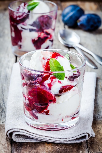 Homemade ice cream with roasted plums in a glass on wooden table