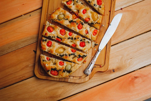 Homemade Italian Focaccia, with tomato and olive oil on a rustic wooden background.