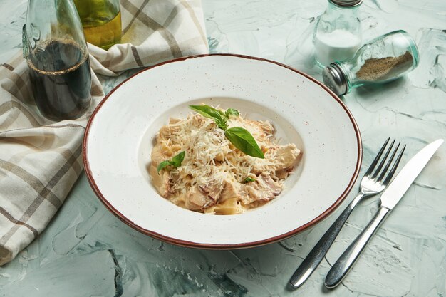 Homemade Italian pasta tagliatelle with white sauce and bacon and turkey, parmesan in a blue plate on a beige background