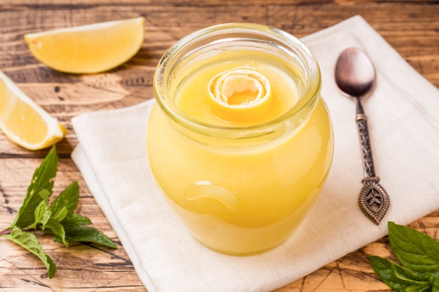 Homemade lemon curd in glass jars with fresh lemons, rustic wooden background