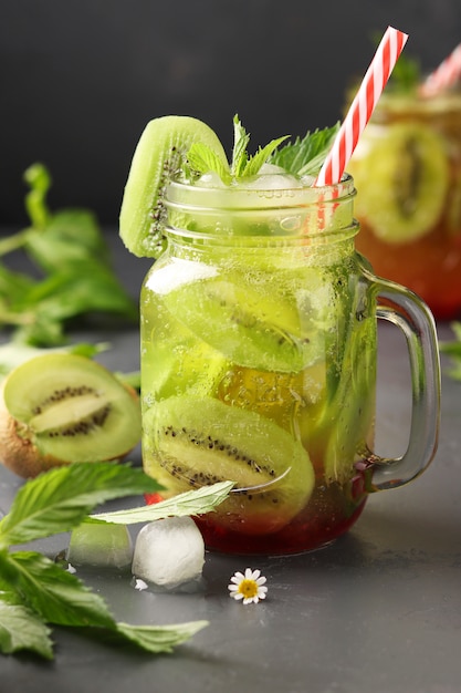 Homemade lemonade with kiwi, lemon and mint in a transparent glass against a dark surface, vertical format