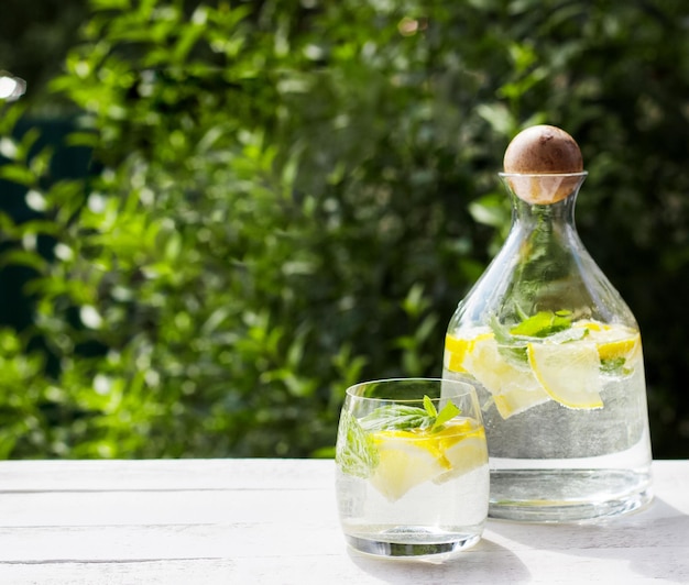 Homemade lemonade with lemon mint and ice cubes in a glass pitcher on the white wood table