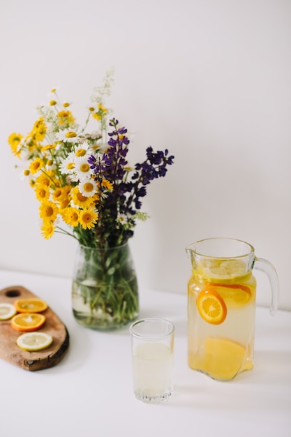 Homemade lemonade with orange and lemon and a bouquet of wild natural flowers on white table