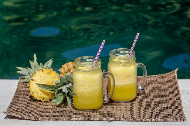 Homemade mango and pineapple smoothie made with coconut milk in two glass mug near swimming pool Island Bali Indonesia Refreshing tropical fruit drink