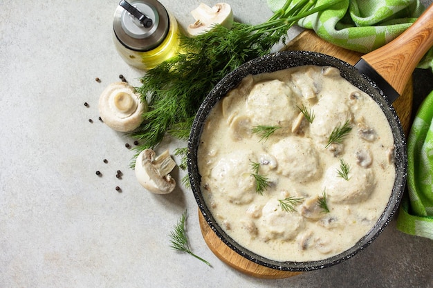 Homemade meatballs in sour cream sauce with mushrooms in a pan on stone or slate table Top view