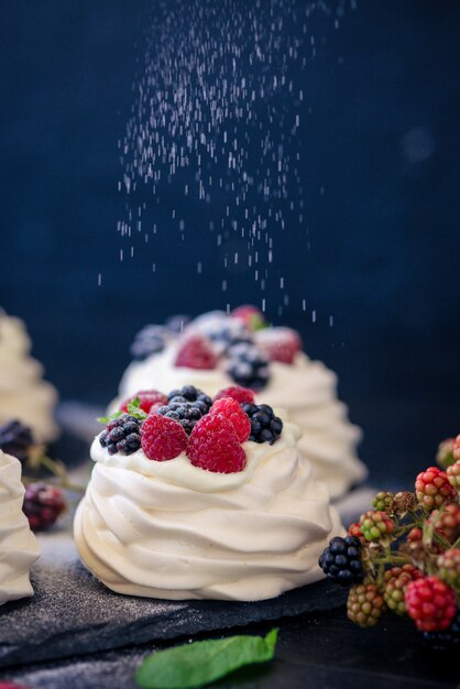 Homemade meringue basis for cake Pavlova with fresh blueberries and BlackBerry and powdered sugar on black concrete