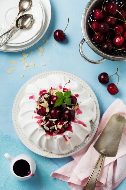 Homemade meringue cake Pavlova with whipped cream, fresh cherry and sauce on light concrete texture surface.Selective focus. Top view,