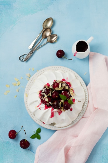 Homemade meringue cake Pavlova with whipped cream, fresh cherry and sauce on light concrete