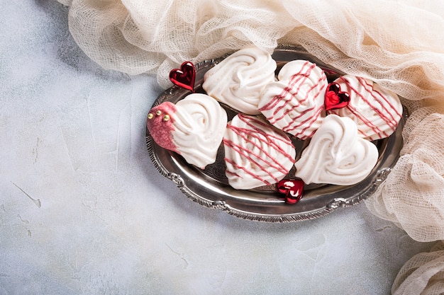 Homemade meringues in heart shape on old metal plate for Valentine's day, top view, copy space