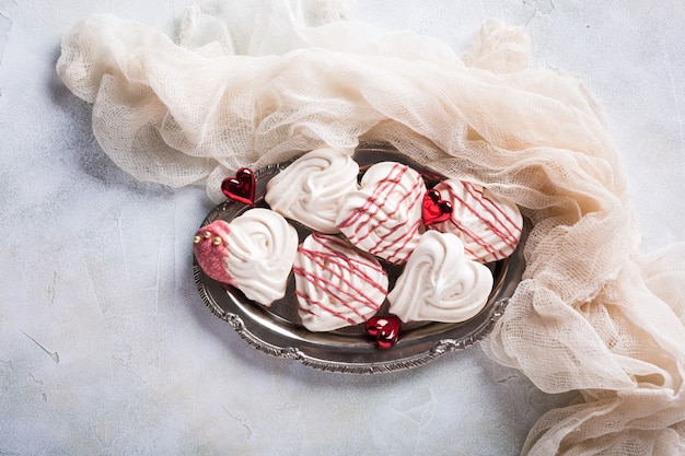 Homemade meringues in heart shape on old metal plate for Valentine's day, top view, copy space