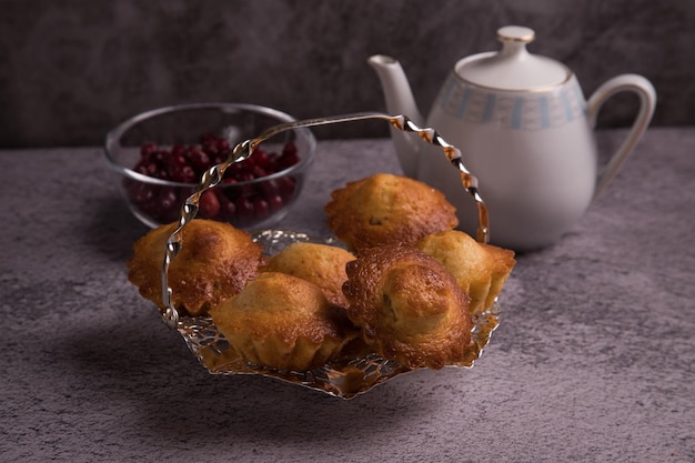 Homemade muffins on an elegant silver tray A teapot with tea and a plate of berries