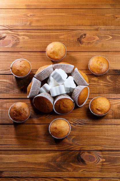 Homemade muffins in paper wrap with marshmallows on wooden board