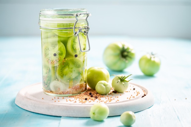 Homemade and natural pickled green tomatoes in jar with spices