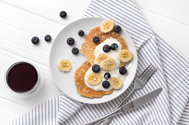 Homemade oatmeal pancakes with yogurt, fresh blueberry and banana at white wooden table.