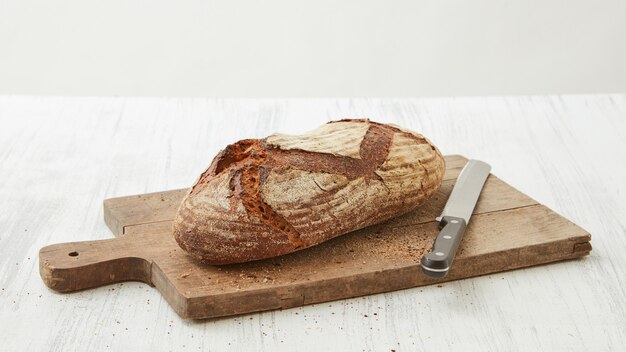 Homemade organic bread on a cutting board with a knife isolated on a white background