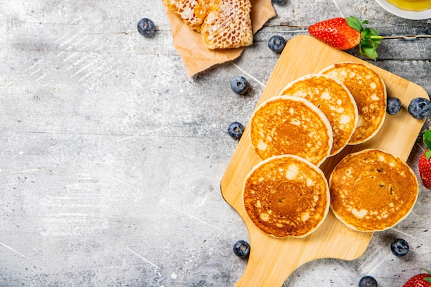 Homemade pancakes on a cutting board with honey and berries