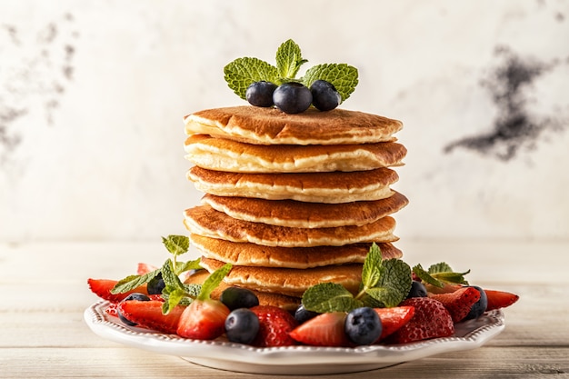 Homemade pancakes with berries and fruit on a white table.