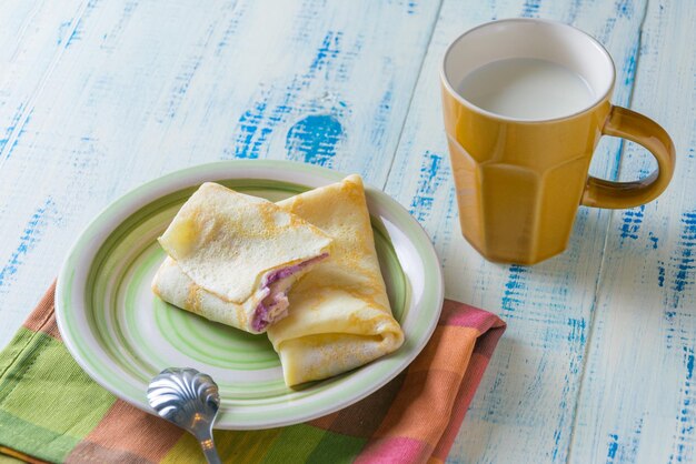 Homemade pancakes with a filling and a cup of milk on a wooden background