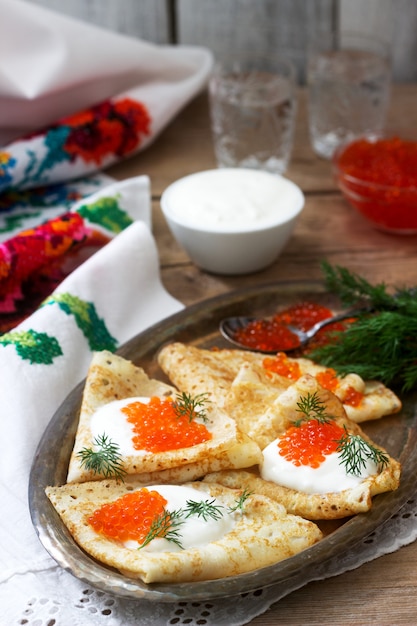 Homemade pancakes with red caviar, sour cream and dill served with vodka. Rustic style.