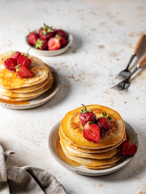 Homemade pancakes with strawberry and honey on kitchen table with napkin and forks American breakfast in rustic style concept