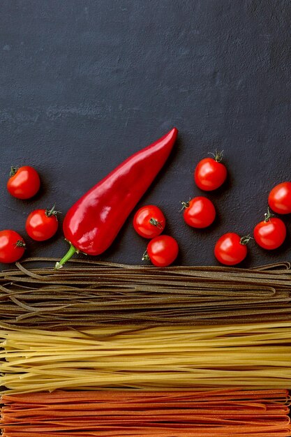 Homemade pasta noodles in different colors with natural vegetable ingredients on a black concrete table