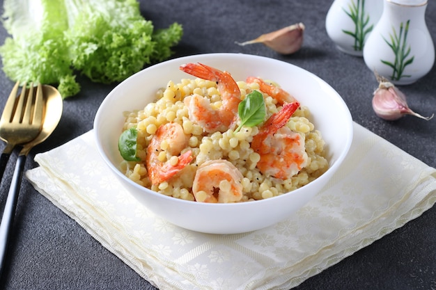 Homemade pasta ptitim with shrimps and basil in white plate on gray background. Close-up