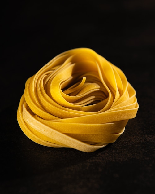 Homemade pasta rolled into a nest on a dark background.