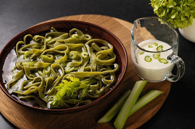 Homemade pasta with broth and celery, sauce in earthenware dish on dark background