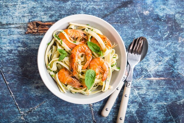 Homemade pasta with fried shrimps and basil on rustic wooden table