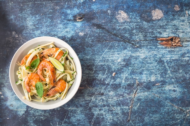 Homemade pasta with fried shrimps and basil on rustic wooden table