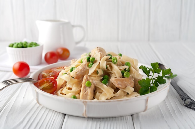 Homemade pasta with green peas, chicken and cream sauce on a white wooden background on a white wooden background