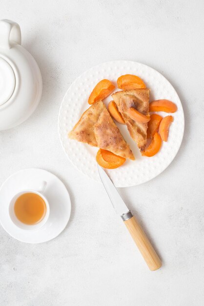 Homemade peach pie with teapot cup of green tea and knife on white background Top view