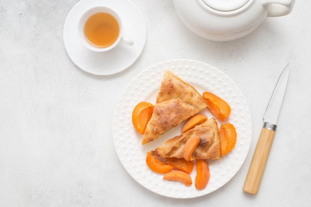 Homemade peach pie with teapot cup of green tea and knife on white background Top view