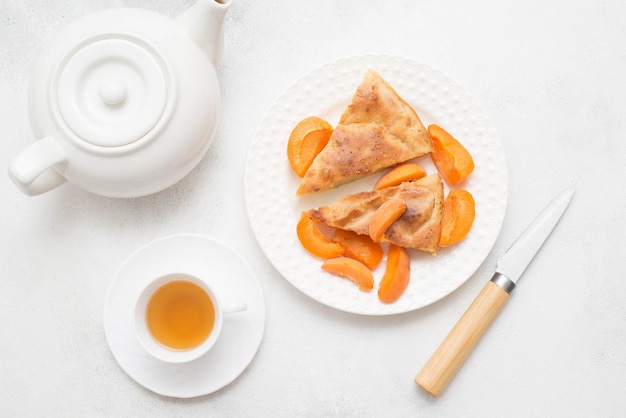 Homemade peach pie with teapot cup of tea knife on white background Top view