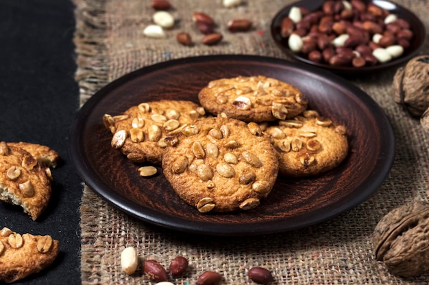 Homemade peanut cookies on a brown plate with raw peanuts in surface