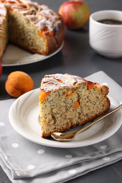 Homemade pie with poppy seeds, apricots and apples with a cup of coffee on a gray background. Vertical arrangement. Close-up