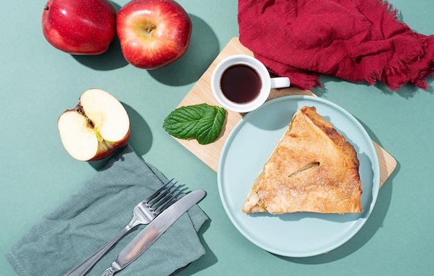 Homemade piece of apple pie with fresh red apples on green table