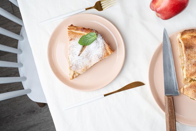 Homemade piece of apple pie with fresh red apples on white table