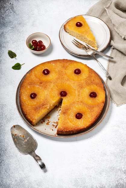 Homemade pineapple upside down cake with candied cherries and a piece cut off on a plate