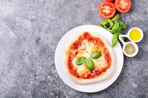 Homemade pizza margherita with mozzerala cheese served with fresh basil, spices oregano and tomatoes over blue texture surface. Top view, flat lay. Copy space