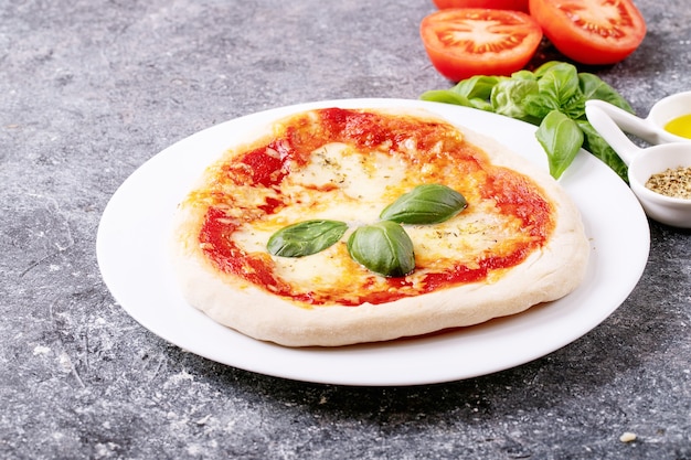 Homemade pizza margherita with mozzerala cheese served with fresh basil, spices oregano and tomatoes over blue texture surface